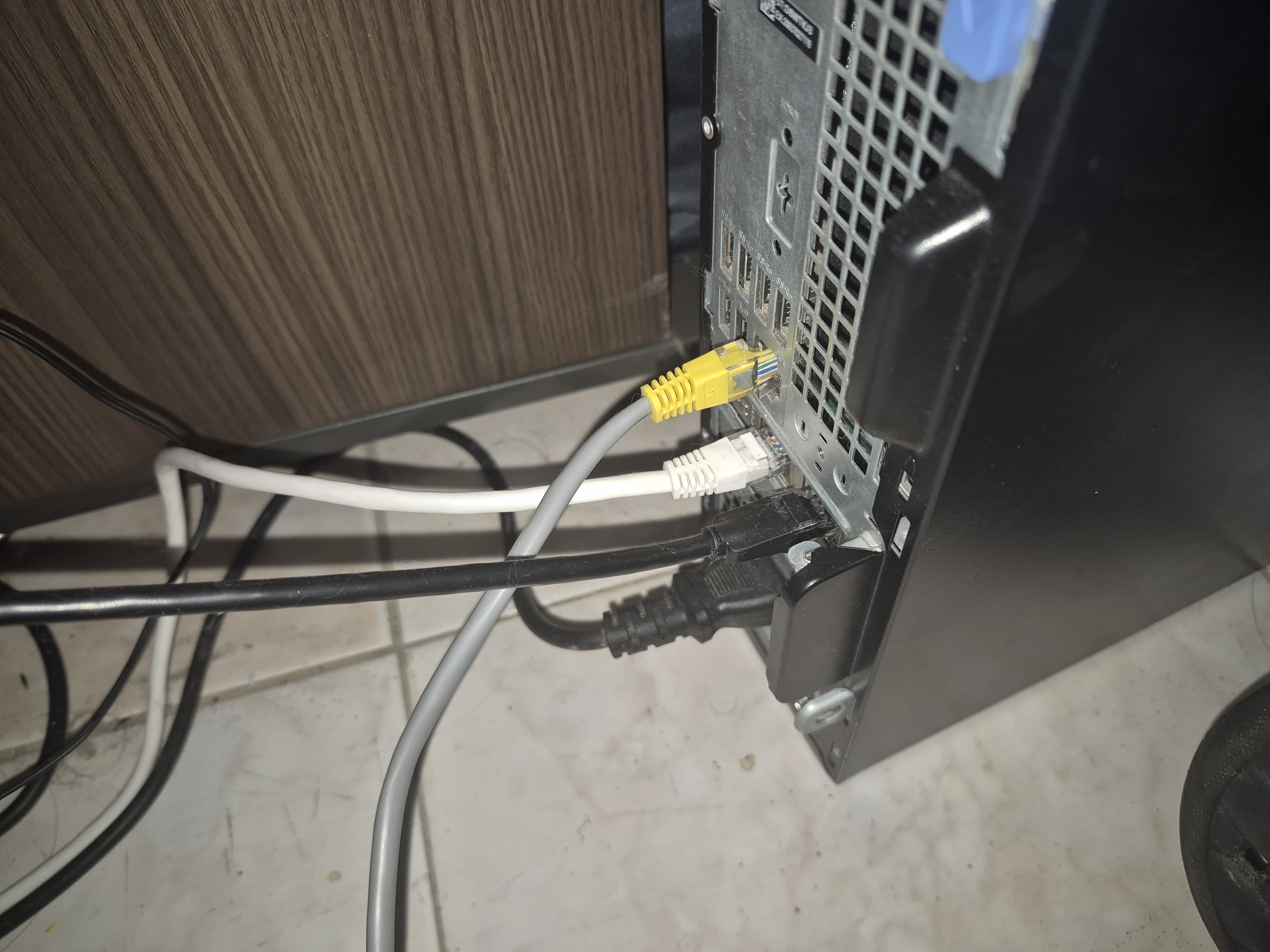 The back of a small form factor PC with USB, Ethernet, and power cables plugged in — a new homelab node being wired up.